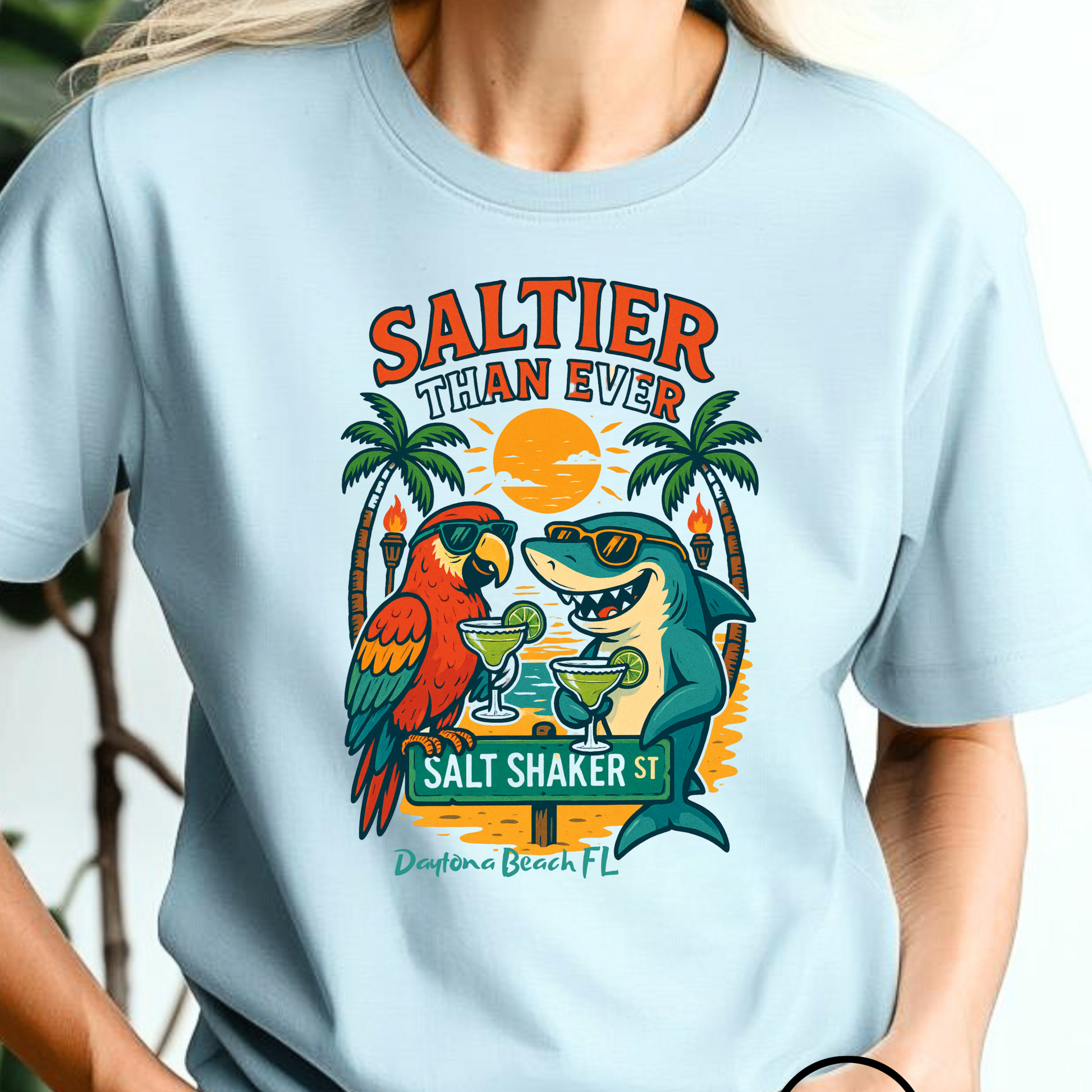 Person wearing a light blue t-shirt with a tropical design featuring a shark, parrot, and palm trees.